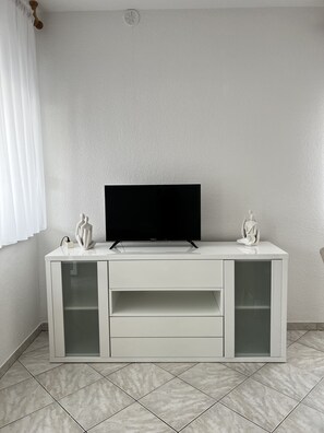A white entertainment unit with a flat-screen TV, two decorative items, and a tiled floor. - Apartment Lavaran 1 in Vir (Vir)