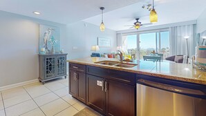 A modern kitchen with dark cabinets, a stainless steel dishwasher, and a large island with a sink. There is a ceiling fan and pendant lighting above the island.