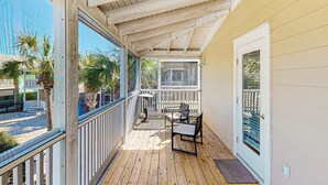 Una terraza de madera con barandal blanco, una puerta con ventana y una pequeña mesa y silla.
