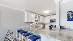 Een moderne keuken met een marmeren aanrechtblad, witte kastjes en blauwe barkrukken.