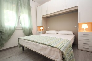 Um quarto com cama, mesa de cabeceira, luminária e guarda-roupa.