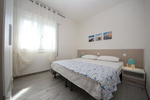 A bedroom with a bed, a nightstand, a lamp, and a window with sheer curtains. - Rosolina Apartment With Parking (Rosolina)