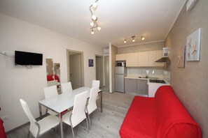 A compact living space with a dining area, kitchenette, and a red sofa. - Rosolina Apartment With Parking (Rosolina)