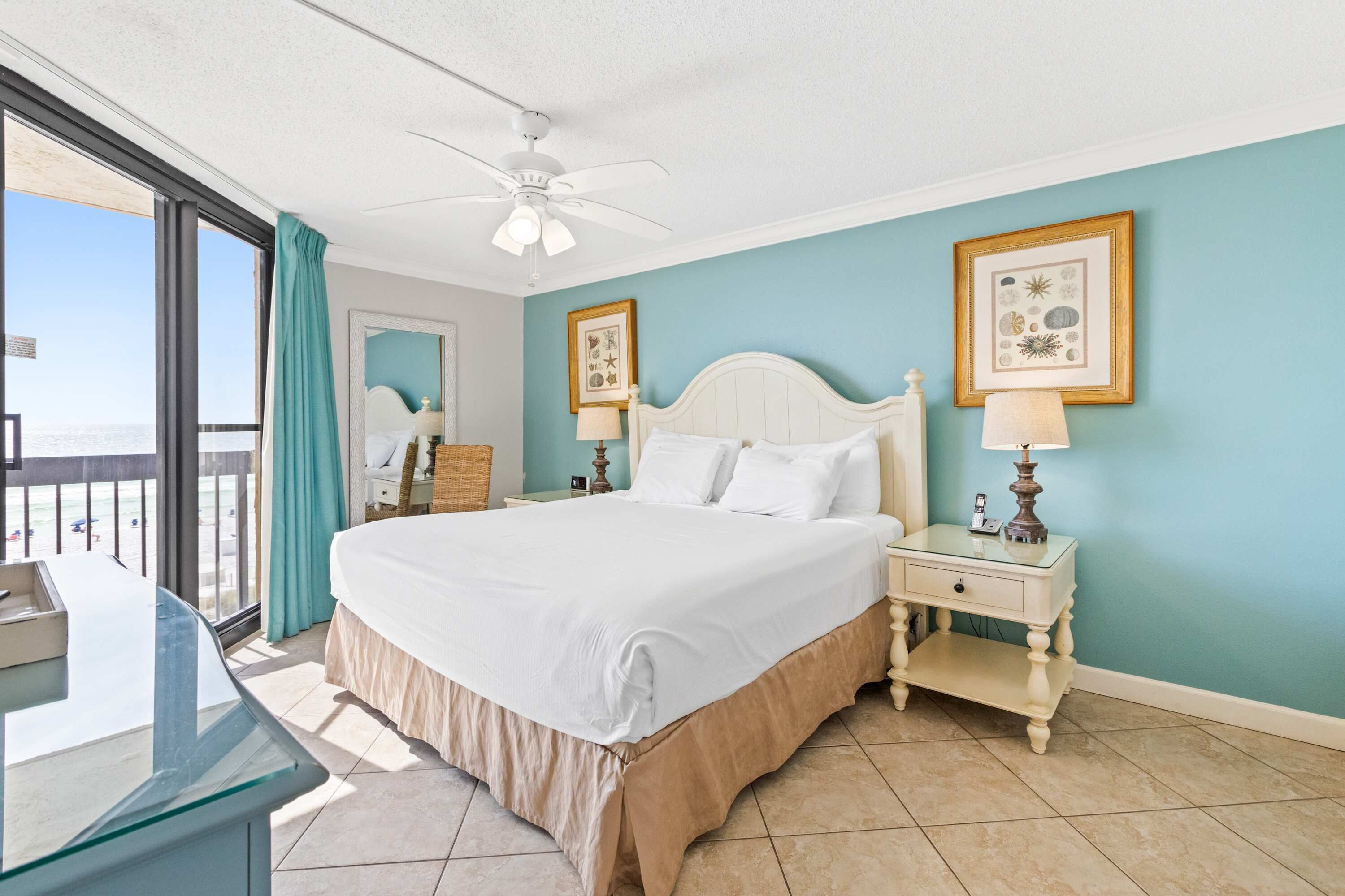 A bedroom with a large bed, a nightstand, a desk, and a ceiling fan.