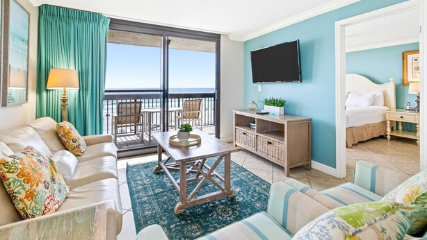 Een goed verlichte woonkamer met een bank, een salontafel en een televisie. Er is een balkon met uitzicht op zee.