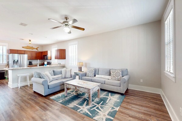 A spacious living room with a large gray sofa, a coffee table, and a kitchen area in the background. - 2-story beach cottage with pools, hot tub, gym, patio, & AC - dog-friendly (Port St. Joe)