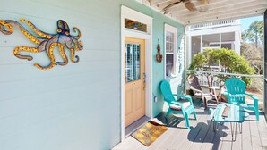 Eine Veranda mit Türkis-farbenen Stühlen, einem Holztisch, Wandkunst mit einem dekorativen Oktopus und einem Deckenventilator.