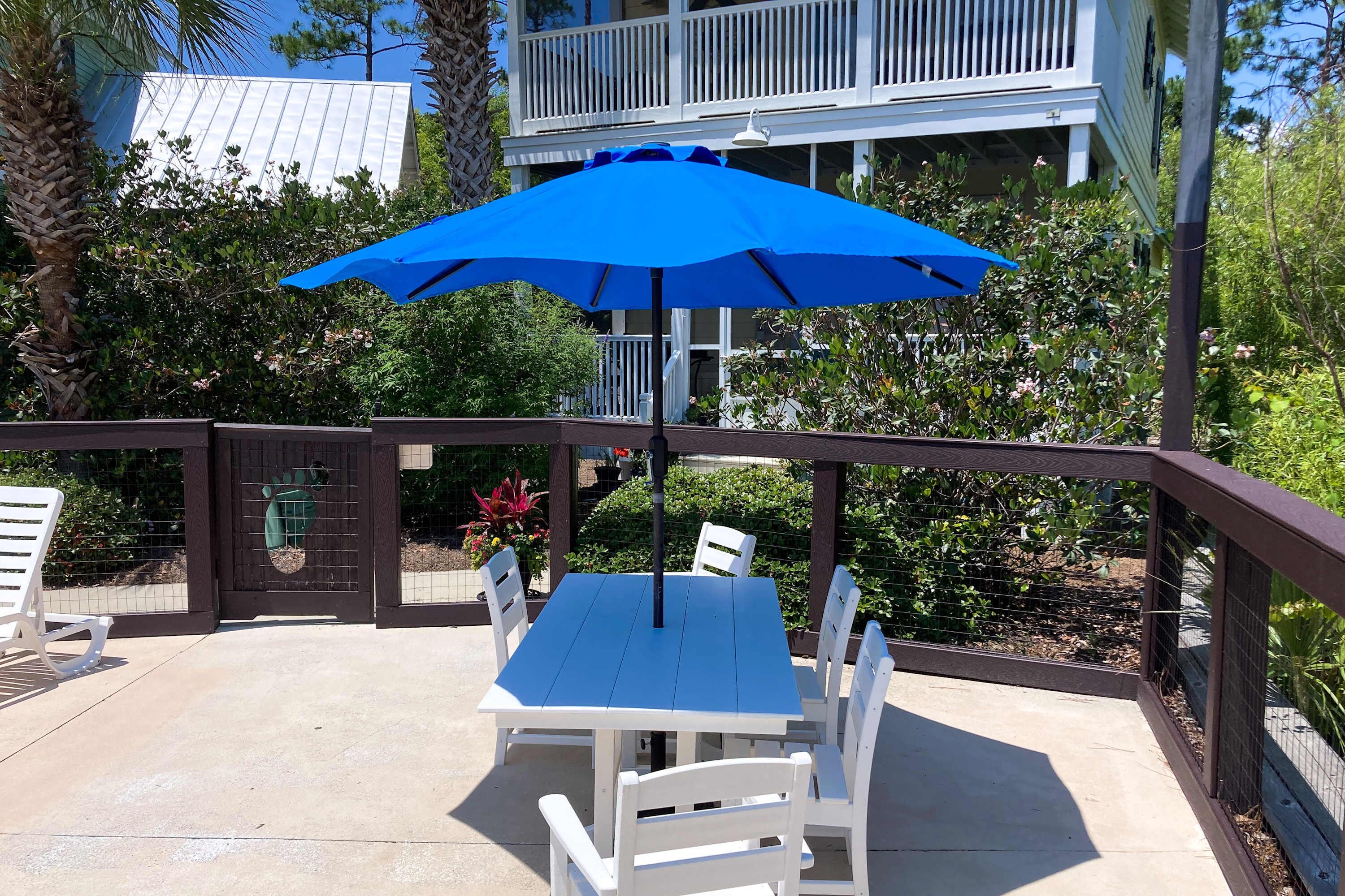 Eine Terrasse im Freien mit einem blauen Sonnenschirm, weißen Stühlen und einem Tisch.