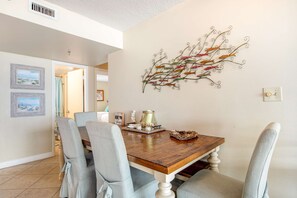 Un coin repas avec une table en bois, des chaises à revêtement gris et un élément décoratif en métal fixé au mur.
