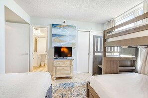 Une chambre avec un lit superposé, une télévision, une commode et un tableau représentant une scène de plage.