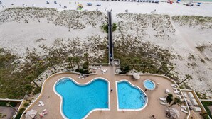 Luchtbeeld van een resort met twee zwembaden, ligbedden en een strandgedeelte.
