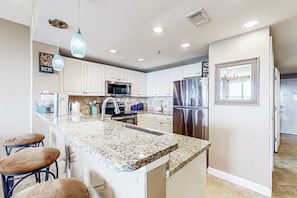 A modern kitchen with white cabinets, stainless steel appliances, and a granite countertop. - Gorgeous, beachfront condo with view of the gulf plus a pool (Destin)
