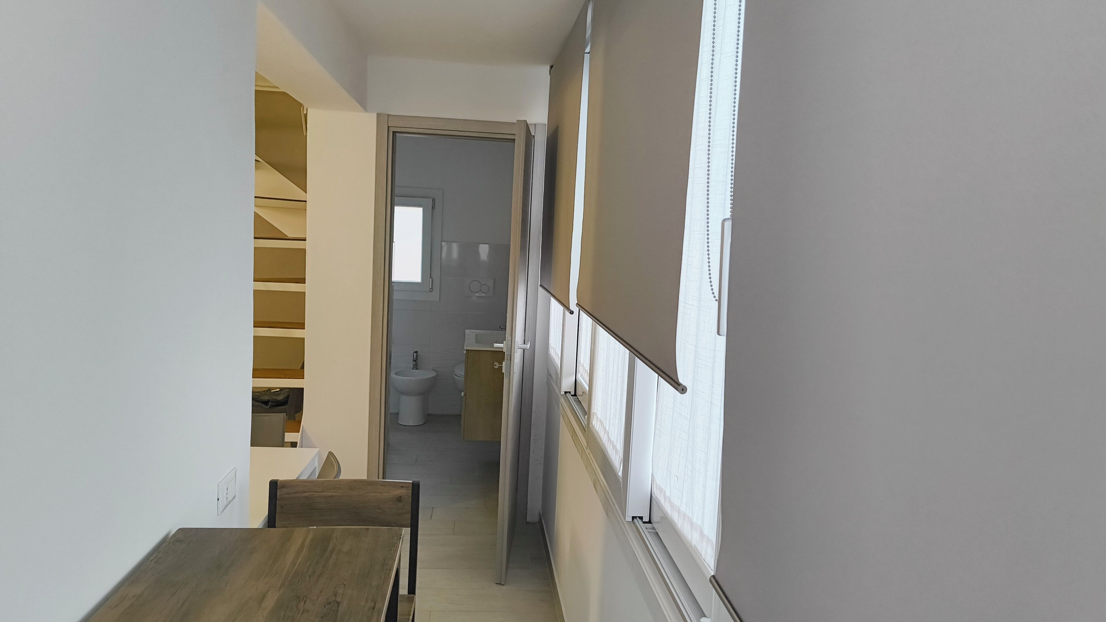 A narrow hallway with a wooden bench, a staircase, and a bathroom visible in the background.