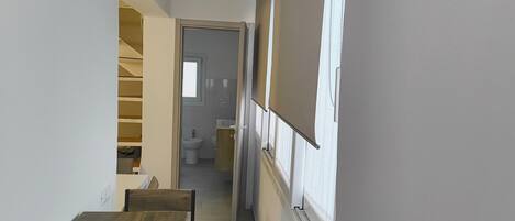 A narrow hallway with a wooden bench, a staircase, and a bathroom visible in the background.