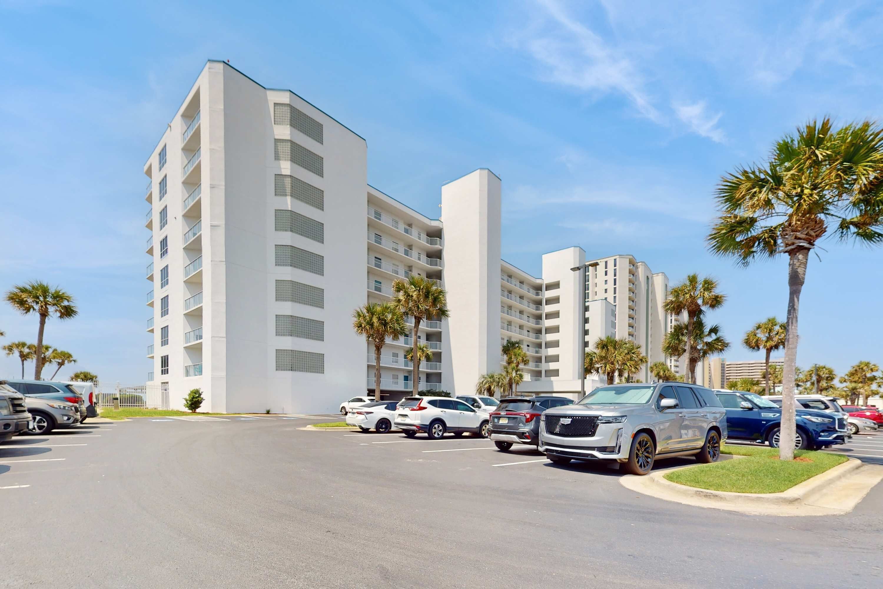 Un parking où sont garés plusieurs véhicules tout-terrain et un grand immeuble blanc, doté de nombreux étages et de balcons.