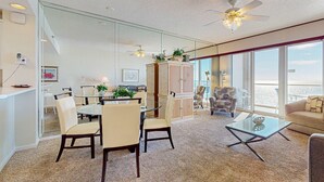A spacious living area with a glass partition, a dining table with chairs, a sofa, a coffee table, and a ceiling fan. - Seaside escape with water view, balcony, pool, pool spa & gym access (Destin)