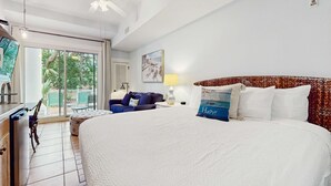 Ett hotellrum med en stor säng, en takfläkt, ett skrivbord med en stol, en soffa och utsikt över omgivningarna genom en skjutdörr.