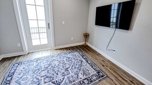 Een kamer met een kamerbreed tapijt, een deur, een wandtelevisie en een klein tafeltje.