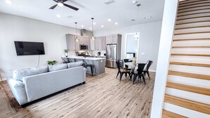 Een moderne keuken met een centraal eiland, een grijze bank, een eettafel met stoelen en een plafondventilator.