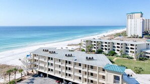 Et hotel ved stranden med flere etager, en parkeringsplads og udsigt over havet.