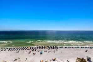 A beach with rows of umbrellas and beach chairs, a lifeguard tower, and a clear view of the ocean. - 14th Floor Welcoming Condo, On-site restaurant, Multiple pools w splash pad (Destin)