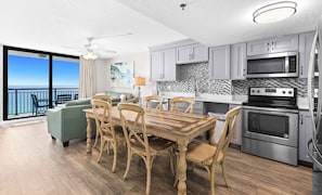 A modern kitchen with a dining area, featuring a large island, stainless steel appliances, and a view to the ocean. - Gulf Front 3BR Condo in Destin with Private Balcony and Resort Pool Access (Destin)