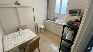 A compact kitchen with white cabinets, a marble countertop, a sink, a microwave, and a small dining area with a chair and table. - Lovely Apartment in Montmartre Paris - Fast Wifi (Paris)