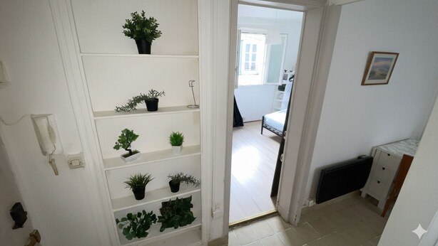 A hallway with white walls, a radiator, and a door leading to a bedroom with a bed and a window. - Lovely Apartment in Montmartre Paris - Fast Wifi (Paris)