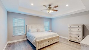 Un dormitorio con cama, cómoda, ventilador de techo y dos ventanas con persianas.
