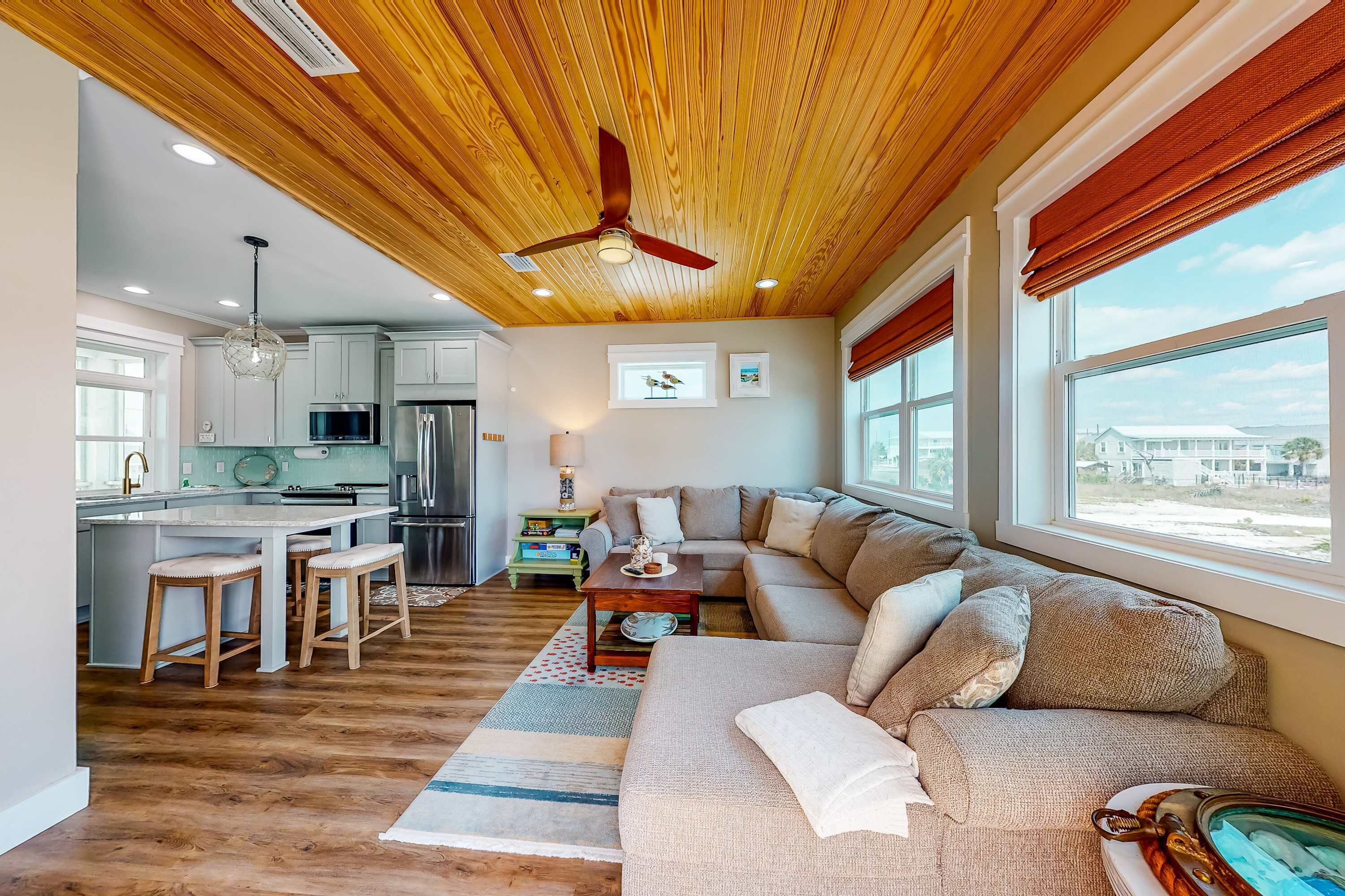 Een moderne woonkamer met een houten plafond, een grote bank, een eethoek en een keuken op de achtergrond.