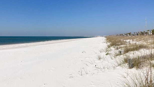A wide, sandy beach with clear blue water and a few buildings in the distance. - Newly built, cottage with historical details, WiFi & central AC - steps to beach (Mexico Beach)