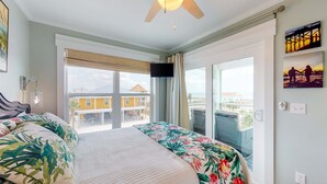 A hotel room with a bed, a ceiling fan, a TV, and a balcony with a view of buildings. - Newly built, cottage with historical details, WiFi & central AC - steps to beach (Mexico Beach)