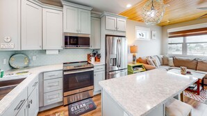 A modern kitchen with white cabinets, stainless steel appliances, and a central island. - Newly built, cottage with historical details, WiFi & central AC - steps to beach (Mexico Beach)
