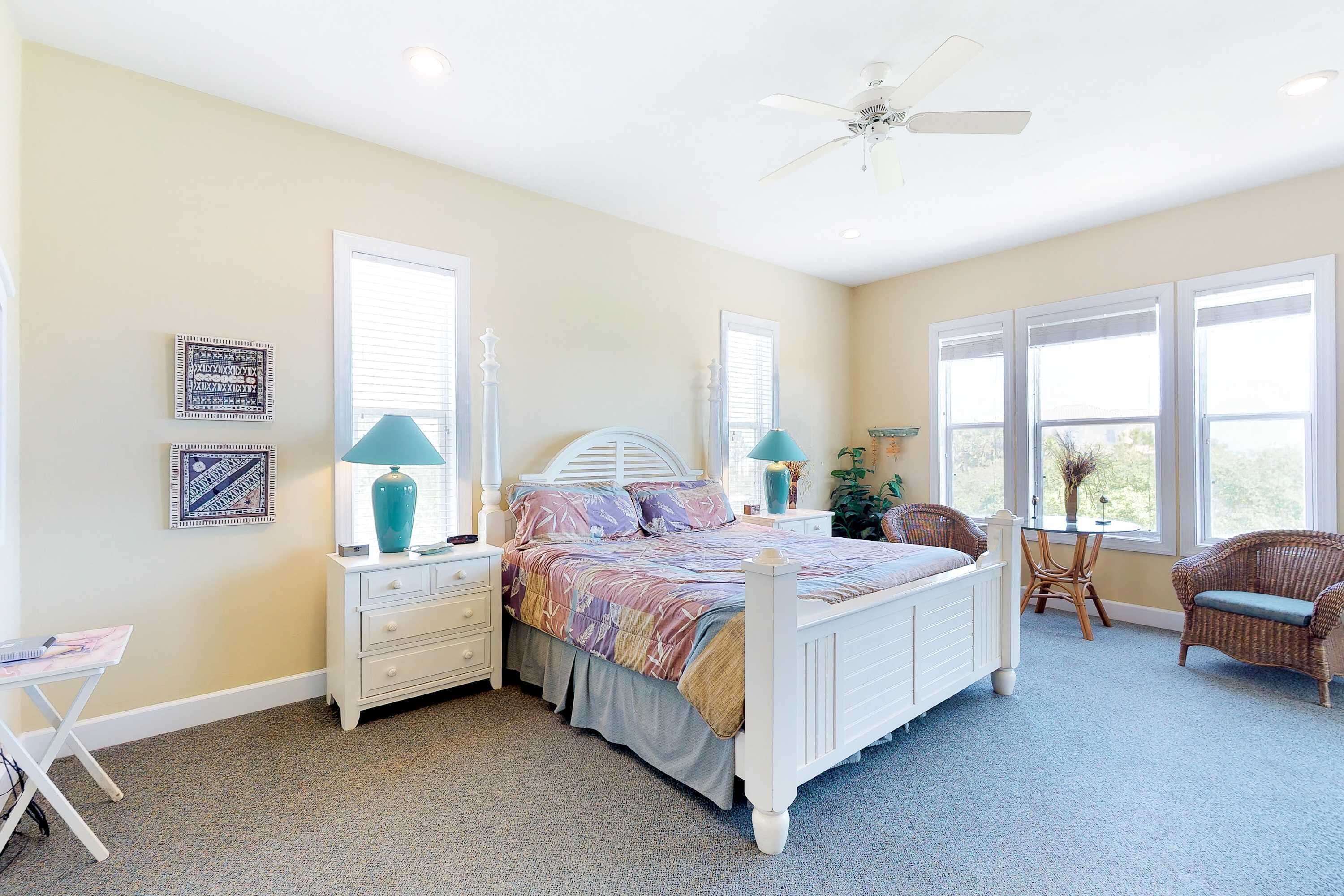 A bedroom with a bed, two nightstands, a chair, a table, and a ceiling fan.