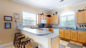 Una cocina con armarios de madera, una isla central con taburetes, un microondas y una ventana con persianas.