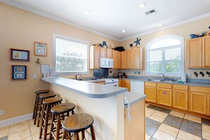 A kitchen with wooden cabinets, a central island with stools, a microwave, and a window with blinds. - Dog-friendly home near the beach with private pool & gym (St. George Island)