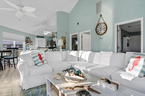 Un salon spacieux avec un canapé d’angle blanc, une table basse agrémentée d’objets décoratifs et un ventilateur de plafond.
