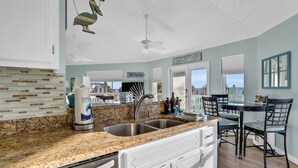 A kitchen with granite countertops, a double sink, white cabinetry, and a dining area with a table and chairs. - Updated beach house with unobstructed gulf views, large deck & outdoor shower (Port St. Joe)