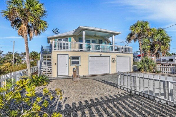 Une maison à deux étages avec un balcon, un garage et une cour clôturée agrémentée de palmiers.