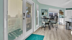 A dining area with a table and chairs, a kitchen area with cabinets and a countertop, and a door with a frosted glass panel. - Updated beach house with unobstructed gulf views, large deck & outdoor shower (Port St. Joe)