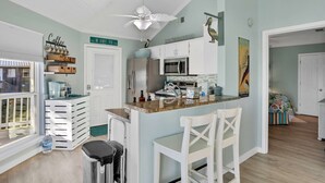 A kitchen with white cabinets, a microwave, and a countertop with various items. There is a ceiling fan, a window with blinds, and a door leading to another room. - Updated beach house with unobstructed gulf views, large deck & outdoor shower (Port St. Joe)