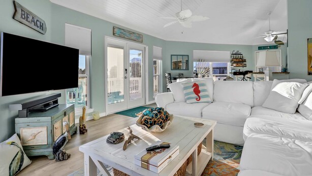 A spacious living room with a large flat-screen TV, a white sofa, and a coffee table with decorative items. - Updated beach house with unobstructed gulf views, large deck & outdoor shower (Port St. Joe)