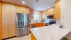 A modern kitchen with stainless steel appliances, wooden cabinets, and a white countertop. - Dog-friendly townhome in private community with pool - near beach (Cape San Blas)