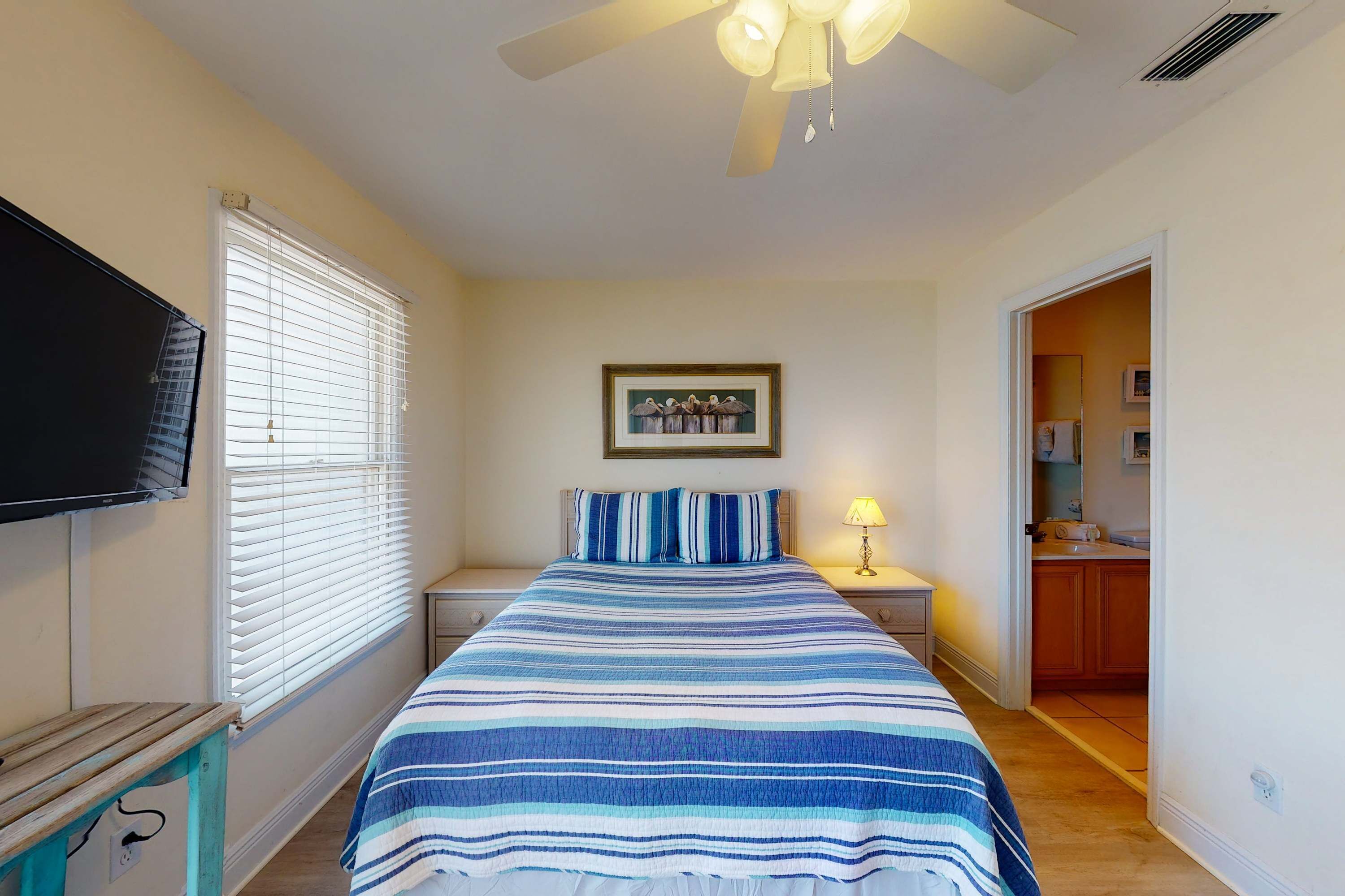 A bedroom with a bed, a television, a ceiling fan, and a framed picture on the wall.