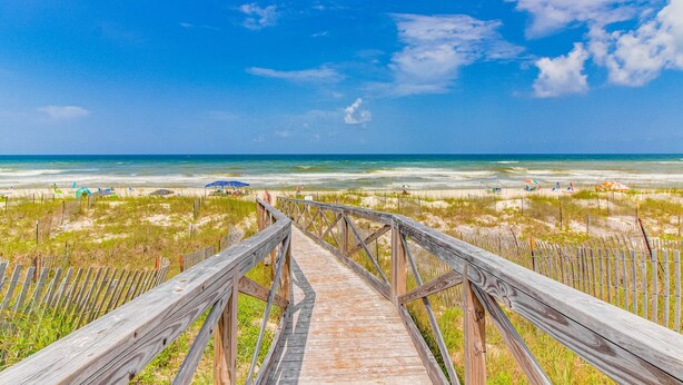 A wooden boardwalk leading to a beach with umbrellas and people in the distance. - Dog-friendly townhome in private community with pool - near beach (Cape San Blas)