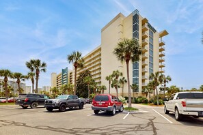 A parking lot with several SUVs parked in front of a hotel with multiple floors and balconies. - Waterfront resort condo w a shared, heated pool, fitness room, & theater (Destin)