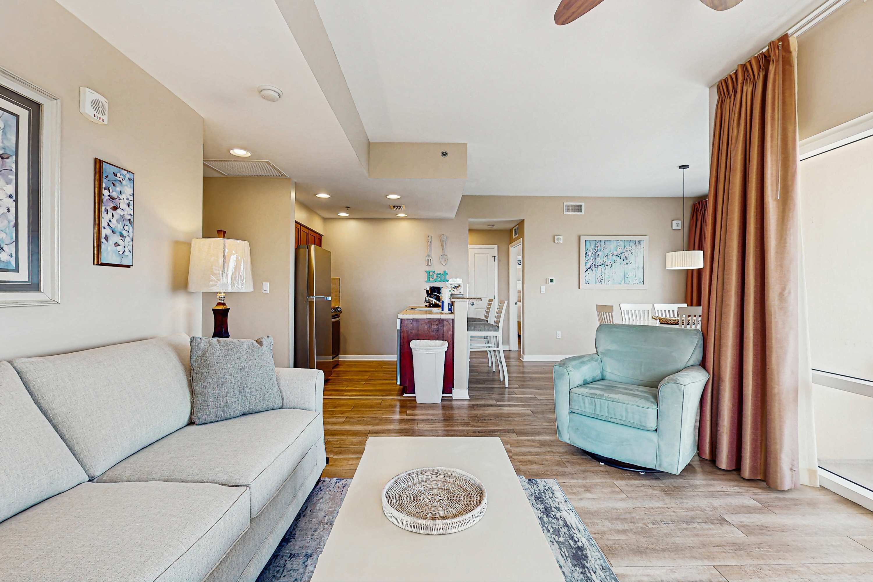 A living room with a sofa, armchair, and coffee table. There is a dining area with a table and chairs.