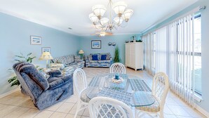 A dining area with a glass-top table, white chairs, and a chandelier. - Pool-side condo with pool, private washer&dryer, walk to beach & free WiFi (Navarre Beach)