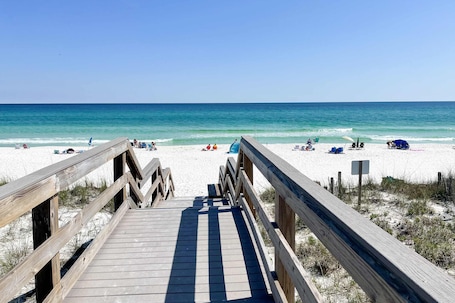 A wooden boardwalk leading to a sandy beach with clear blue water.