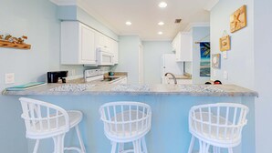 A kitchen with white cabinets, a countertop, and three white bar stools. - Pool-side condo with pool, private washer&dryer, walk to beach & free WiFi (Navarre Beach)